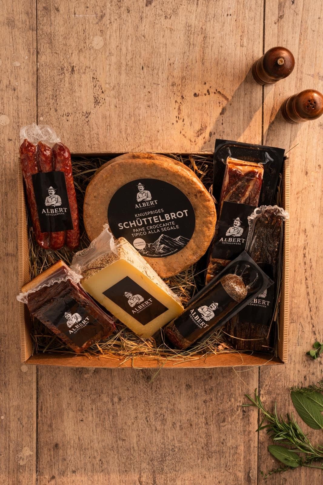 Holzkiste mit Schüttelbrot, Käse, Speck, Salami und Kaminwurzen auf Stroh, von oben
