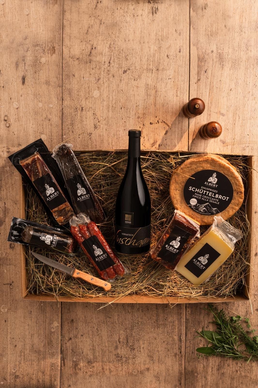 Holzkiste mit einer Flasche Rotwein, Speck, Salami, Käse, Schüttelbrot und Speckmesser