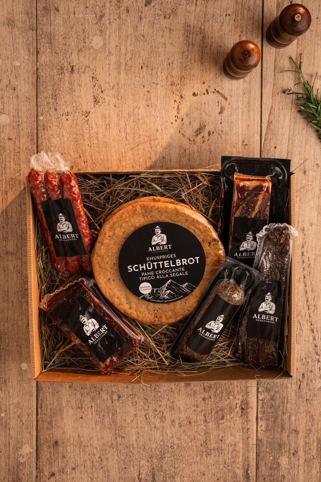 Kleine Südtiroler Genussbox mit Schüttelbrot, Speck, Kaminwurzen und Salami auf Stroh, von oben