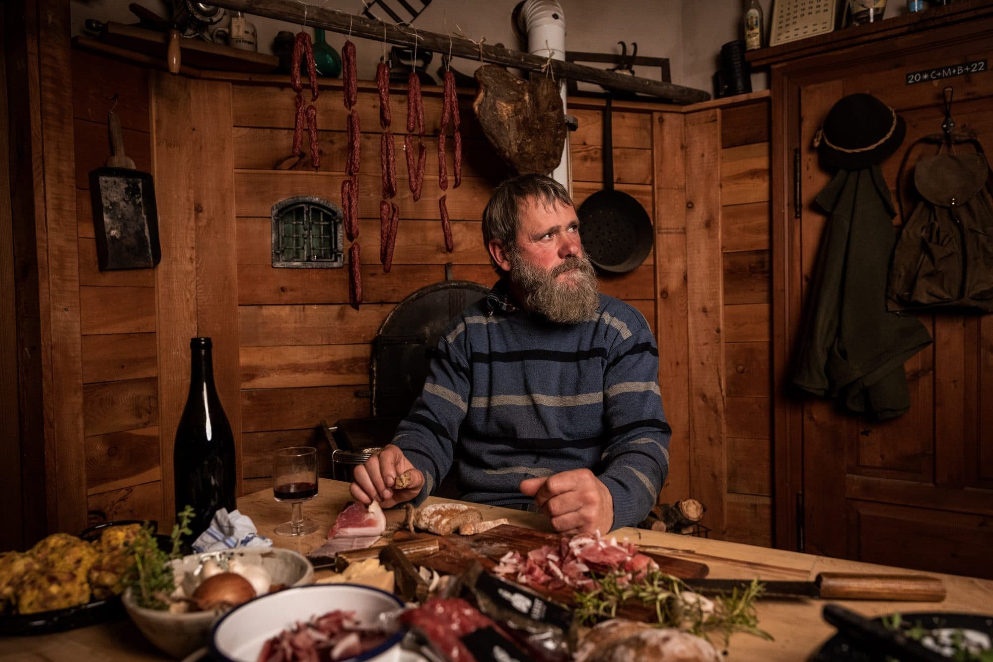 Der Mensch hinter Albert Genusswerk sitzt in der Stube an einem gedeckten Tisch mit Speck und Brot